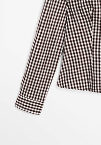 Chemise à manches longues avec motif à carreaux noir et blanc sur fond blanc uni, montrant une manche et une partie du torse.