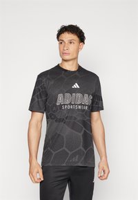T-shirt desportivo Adidas de mangas curtas, preto, com padrão texturizado, logótipo branco e gola redonda. Combinado com calças pretas.