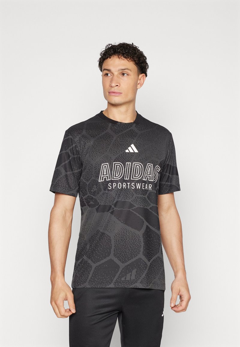 T-shirt desportivo Adidas de mangas curtas, preto, com padrão texturizado, logótipo branco e gola redonda. Combinado com calças pretas.