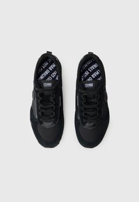 Chaussures de sport noires avec un mélange de matériaux en maille et en daim, superpositions texturées, lacets plats, ainsi qu'une semelle intérieure et une languette avec logo.