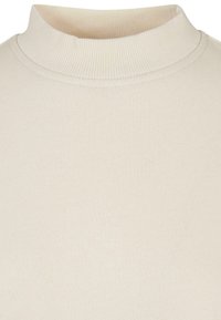 Krémový svetr s dlouhým rukávem a vysokým límcem, vyrobený z měkké, texturované tkaniny. Minimalistický design, žádné viditelné vzory nebo akcenty.