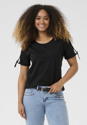 Black T-shirt with a round neck, short sleeves, and adjustable ties at the cuffs. Paired with light blue jeans and a black belt.