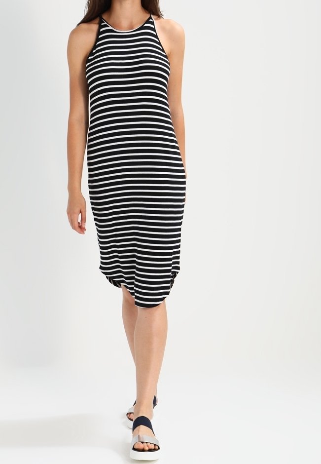 Femme marchant, portant une robe midi sans manches rayée horizontalement noir et blanc et des sandales noires avec des semelles blanches.