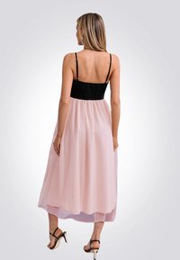 Roze maxi-jurk met een zwarte smocked borststuk en dunne bandjes. De vloeiende rok heeft een transparante textuur en valt tot halverwege de kuit. Hoge sandaaltjes zijn inbegrepen.