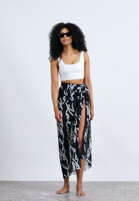 Gonna avvolgente in bianco e nero con motivo a righe e uno spacco alto, abbinata a un crop top bianco. Tessuto leggero e trasparente, legata in vita.