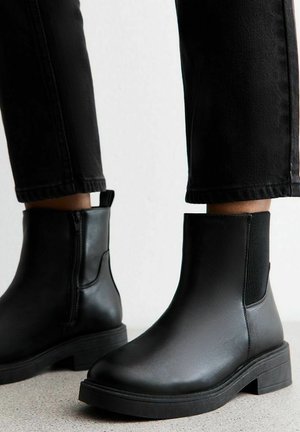 Bottes noires à la cheville en cuir lisse, avec des panneaux latéraux élastiques, une semelle texturée et un petit talon carré.