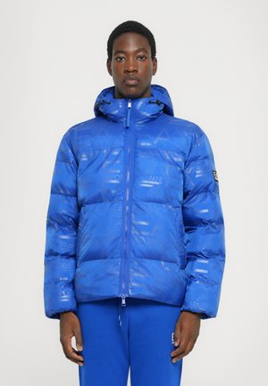 Blue puffer jacket with a glossy finish, featuring an embossed logo pattern, hood, and zip closure. Paired with matching blue pants.