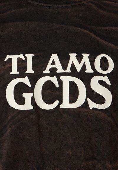 Musta särk, millel on silmapaistev valge tekst, mis ütleb "TI AMO GCDS." Kangas näeb välja pehme ja sujuva tekstuuriga.