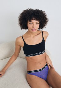 Zwarte bralette met dunne bandjes, voorzien van een witte "HUGO" band. Gecombineerd met paarse kanten slip, ook met een zwarte "HUGO" tailleband.