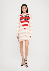 Abito a maniche lunghe a righe in rosa chiaro e bianco, con un cuore rosso e il logo nero "MOSCHINO" sulla parte anteriore. Tessuto morbido, vestibilità rilassata.