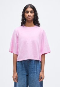 Sweat-shirt rose court à manches courtes, en tissu doux, avec un col rond et un ourlet côtelé. Associé à un pantalon ample en denim bleu.