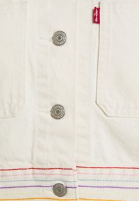 White denim fabric features silver hardware buttons. Colorful horizontal stripes in red, pink, blue, and yellow are along the hem.