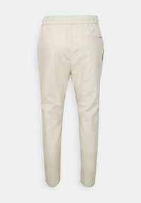 Beige cotton trousers with an elastic waistband, slim shape, and back pocket. Smooth texture with minimal stitching details.