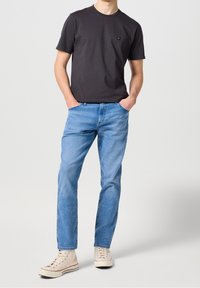 Svart bomullströja med en liten logotyp, i kombination med ljusblå denimjeans och beige sneakers. Avslappnad passform, rak benmodell, enkelt mönster.