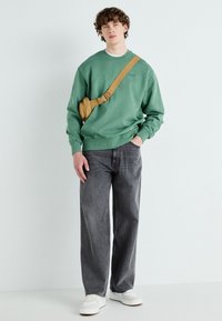 Groene sweatshirt, grijze wijde jeans, witte sneakers en een tan schoudertas. De sweatshirt heeft geribbelde manchetten en een ronde halsontwerp.