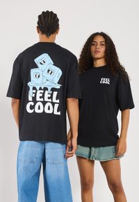 Schwarze Baumwoll-T-Shirts im Übergrößenfit, mit einem blauen Cartoon-Eiswürfel-Graphic sowie dem Text "FEEL COOL" auf der Vorder- und Rückseite.