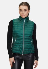 Grön vadderad väst med hög krage, framzip, och två fickor med dragkedja. Slät textur, horisontellt kviltat mönster, lättviktsdesign.