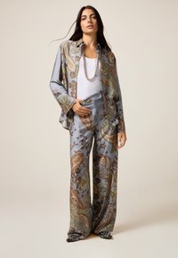 Completo in seta con motivo paisley blu, composto da una blusa dal taglio morbido con maniche lunghe e pantaloni a gamba larga, impreziosito da una leggera lucentezza.