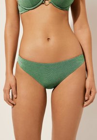 Groene hipster bikini onderkant van een glanzend, gestructureerd materiaal. Heeft een gematigde snit en een soepele tailleband zonder zichtbare hardware.