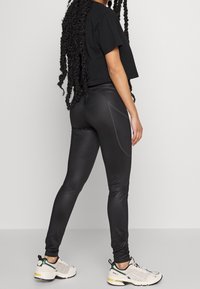 Svarta atletiska leggings med en slät textur och åtsittande design, som har kontrasterande sömmar och en sidologotyp. Bärs med en kortärmad svart tröja och sneakers.