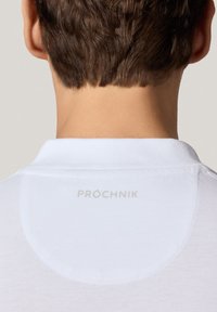 Biała koszulka polo z teksturowanej tkaniny, featuring płaskim kołnierzykiem i małym, jasnym logo "PROCHNIK" na plecach.