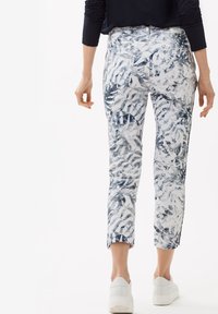Pantalon blanc avec un motif de feuilles bleues, coupé à la cheville. Associé à des baskets blanches. Tissu lisse avec un léger éclat.