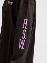 Crna košulja dugih rukava s ružičastim natpisom "H.S.W." na rukavu i malim logom "hummel SPORTSWEAR" blizu ramena.