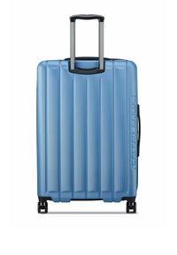 Valise rigide bleu clair, avec des rainures verticales, une poignée noire et des roulettes pour la mobilité. Nom de la marque embossé sur le côté.