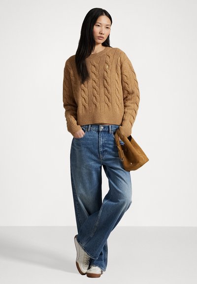 Suéter beige de punto grueso, vaqueros de pierna ancha azul, bolso de ante color tostado y zapatillas grises. Enfoque en la textura, el color y el ajuste relajado.