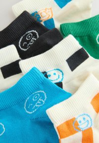 Chaussettes chevilles colorées avec des motifs de visages souriants et des rayures contrastées en noir, vert, bleu, orange et blanc superposées.