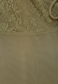 Tissu en dentelle beige avec motifs floraux en haut, se transformant en un matériau en maille lisse en dessous. Texture douce sur toute la surface.
