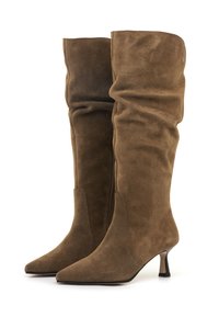 Bottes en cuir suédé marron, arrivant aux genoux, avec des tiges décontractées, des bouts pointus, des zips sur le côté et de petits talons kitten sur fond blanc.