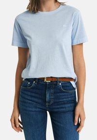 Lichtblauwe katoenen t-shirt met korte mouwen, ronde halslijn en een klein logo op de borst. Draagt met donkerblauwe spijkerbroek en een bruine riem.