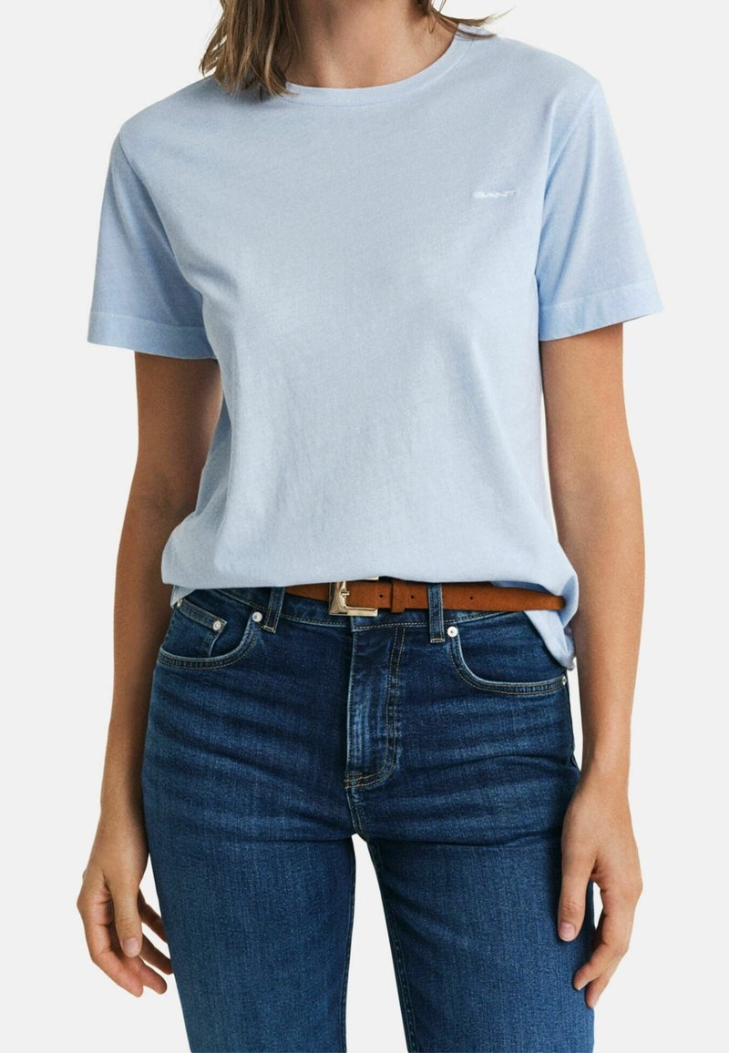 Lichtblauwe katoenen t-shirt met korte mouwen, ronde halslijn en een klein logo op de borst. Draagt met donkerblauwe spijkerbroek en een bruine riem.