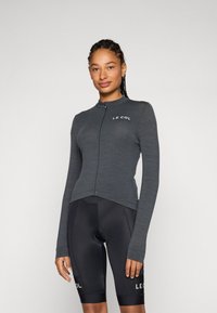 Mørkegrå langermet sykkeltrøye med glidelås foran og høy krage. Har en slim fit og logo, kombinert med svarte sykkelshorts.