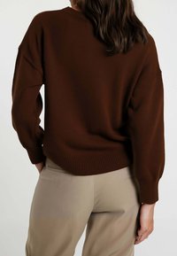 Maglione a coste marrone dal taglio morbido, con spalle scese e scollatura arrotondata, abbinato a pantaloni beige classici.