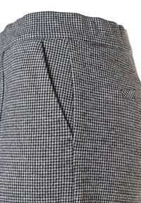 Close-up van zwart-wit houndstooth-gepatenteerde broek met tailleband en schuine zijzakdetails.