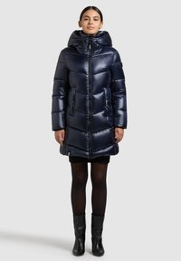 Tamsiai mėlynas pūstas paltas su gaubtu, užtrauktuku ir priekinėmis kišenėmis. Turi siuvinėtą dizainą su lygiu, blizgiu paviršiumi.