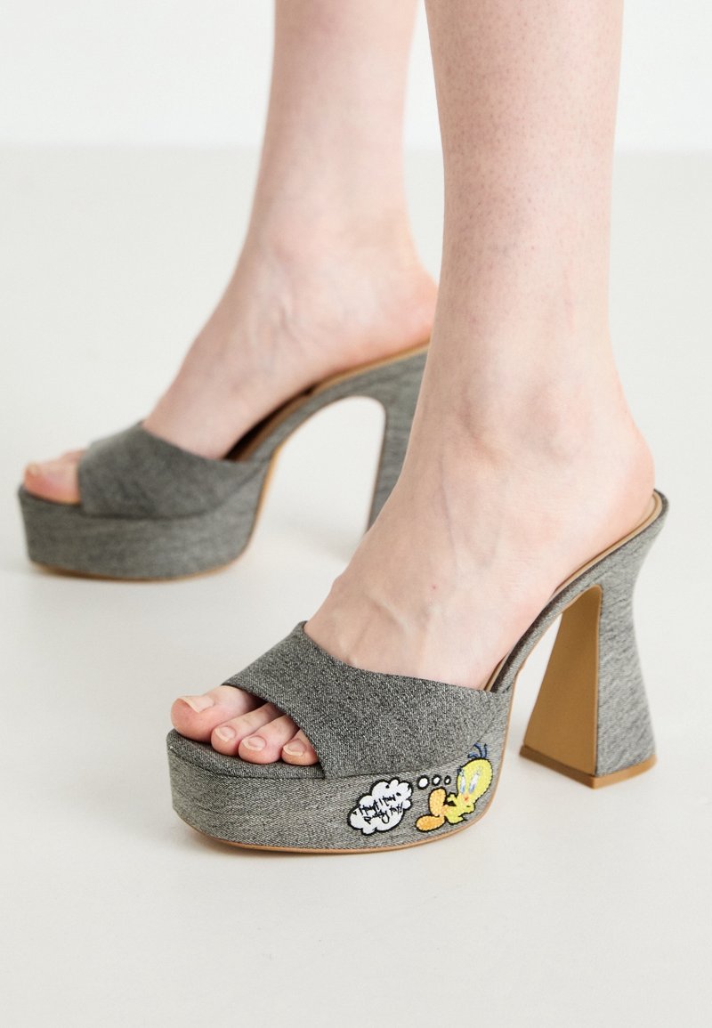 Talons compensés en tissu gris avec un talon bloc élevé. Présentent un design à brides croisées et un personnage brodé coloré sur le côté.