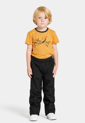 Oranje katoenen T-shirt met zwart octopusontwerp, gecombineerd met zwarte broeken met elastische taille en witte sneakers. Kind staat tegen een witte achtergrond.