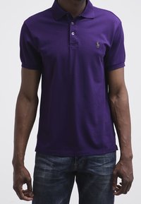 Lila pikétröja i bomull med klassisk krage och treknapplåsning, med en liten broderad logotyp på vänstra bröstet.