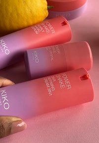 Tre prodotti per la cura della pelle KIKO Milano in contenitori a gradiente rosa e viola, caratterizzati da forme arrotondate e testo bianco. Include un limone sullo sfondo.