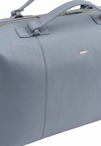 Sac de voyage en cuir pebble gris avec deux poignées supérieures, une fermeture éclaire et un petit accent logo métallique. Texture lisse et forme rectangulaire.