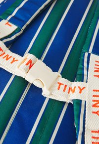 Tissu rayé bleu et vert avec des bretelles blanches et orange et une boucle en plastique. La texture semble lisse et légèrement brillante.
