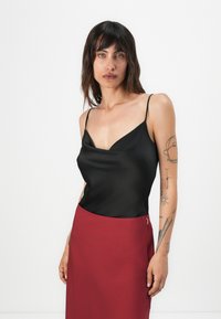 Camisole en satin noir avec des fines bretelles, dotée d'un décolleté en V. Associée à une jupe bordeaux ajustée. Texture lisse, design épuré.