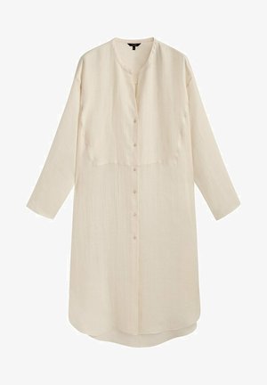 Robe longue beige clair semi-transparente boutonnée avec des manches larges portée sur un pantalon en crochet assorti et un collier visible.