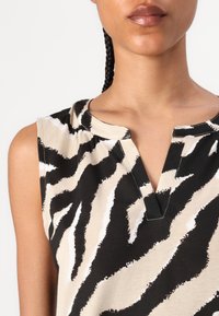 Top a maniche corte beige con motivo zebra bianco e nero. Presenta un collo a V e dettagli arricciati al colletto. Tessuto di cotone morbido.