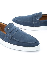 Mocasines de ante azul con suela de goma blanca, que presentan costuras prominentes y un acento cosido en la parte delantera. Forro interior suave.