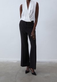 Vit satinskortsärm top med draperad framtill, i kombination med högmidjade svarta vida byxor och svarta spetsiga klackskor.