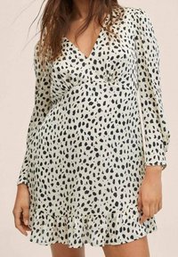 Robe à manches courtes et décolleté en V, de couleur vert clair avec des taches abstraites noires, dotée d'un ourlet froncé et d'une coupe légèrement ample. Texture de tissu lisse.